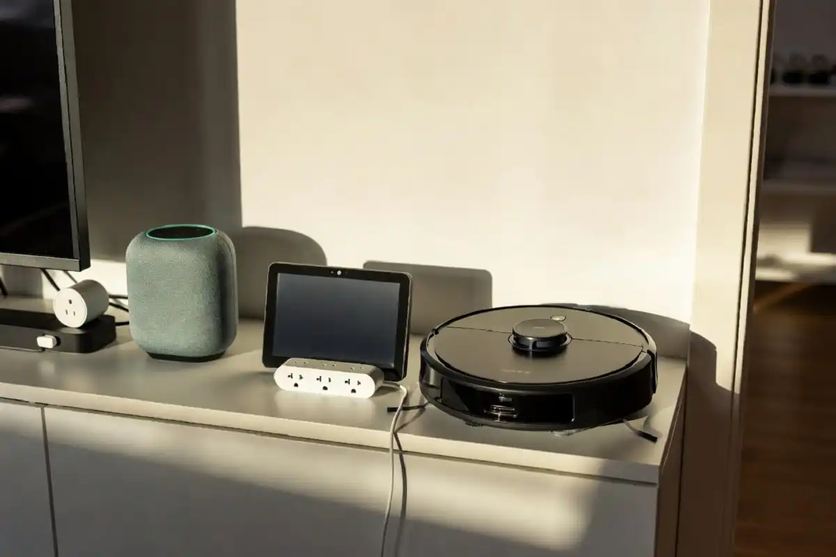 A collection of the best home gadgets including a smart speaker, robot vacuum, and smart display on a modern living room shelf