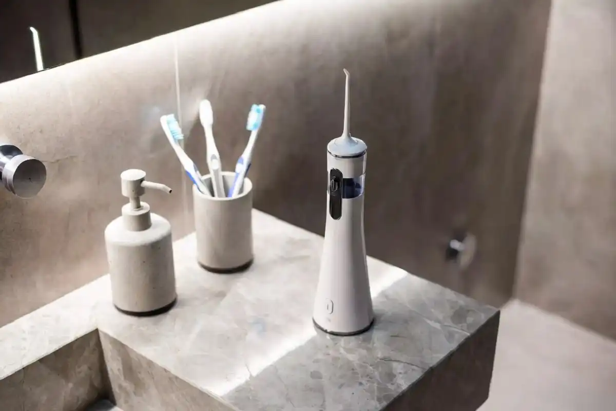A white electric water flosser sitting on a clean bathroom counter next to a toothbrush holder