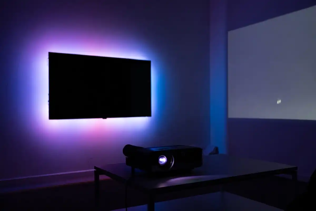 Smart LED strips behind TV and mini projector in modern living room electronics setup