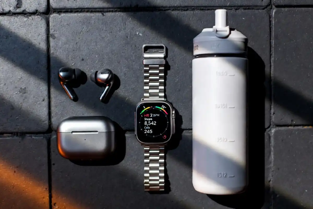 Fitness gadgets including a smartwatch and wireless earbuds on a gym surface