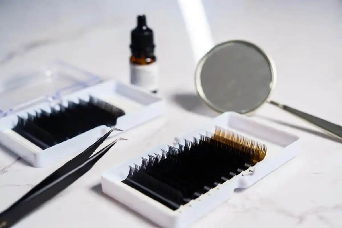 Professional lash tech tools laid out neatly including tweezers, lash trays, and adhesive