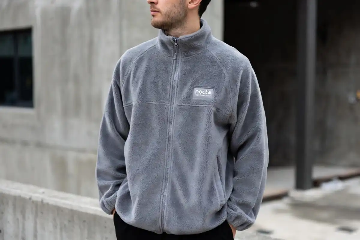 Male model wearing nocta tech fleece in grey in an urban street setting