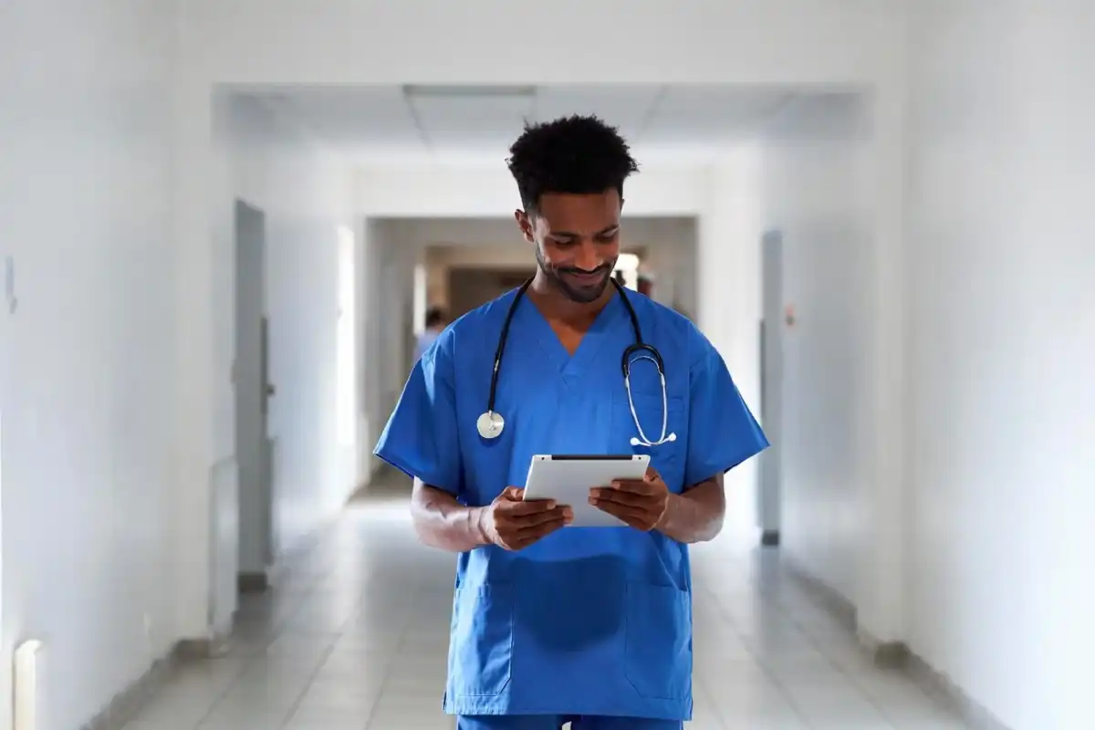 A radiology tech professional in a hospital corridor holding a tablet and reviewing patient imaging data