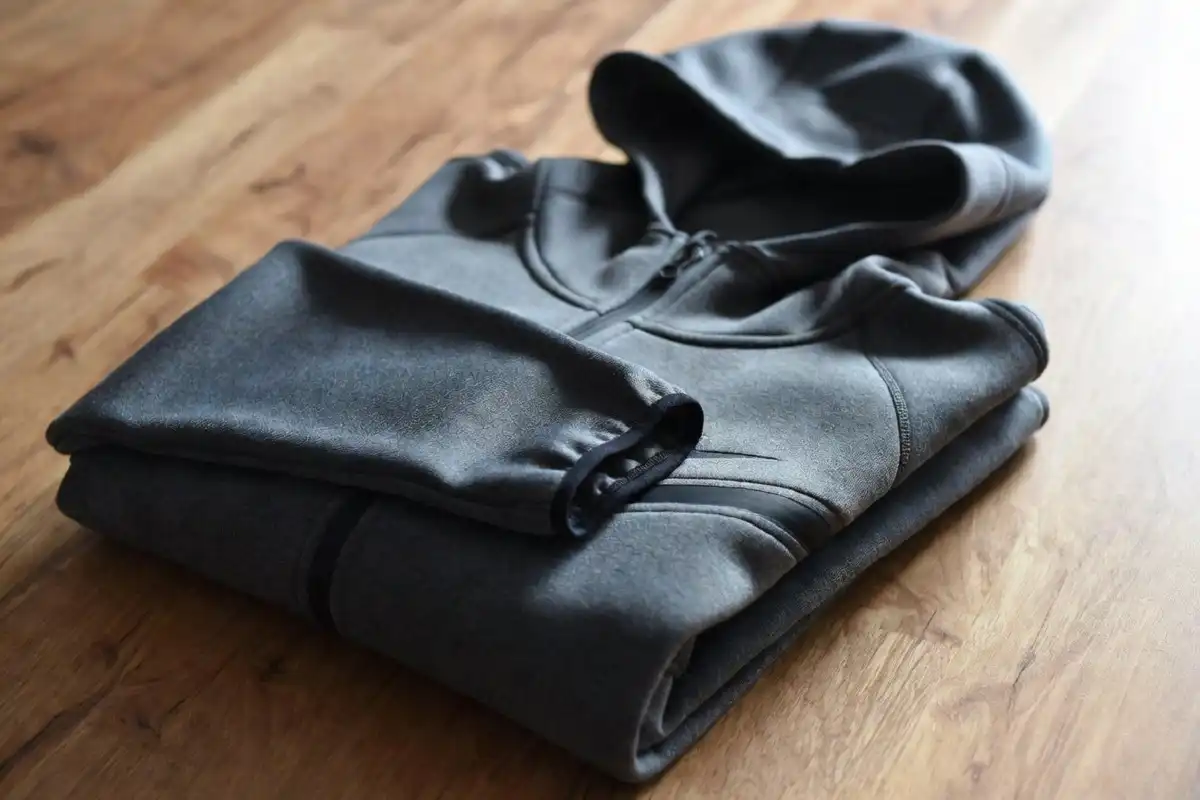 Neatly folded dark Nike Tech Fleece hoodie on a wooden surface showing reflective cuff and zip detail