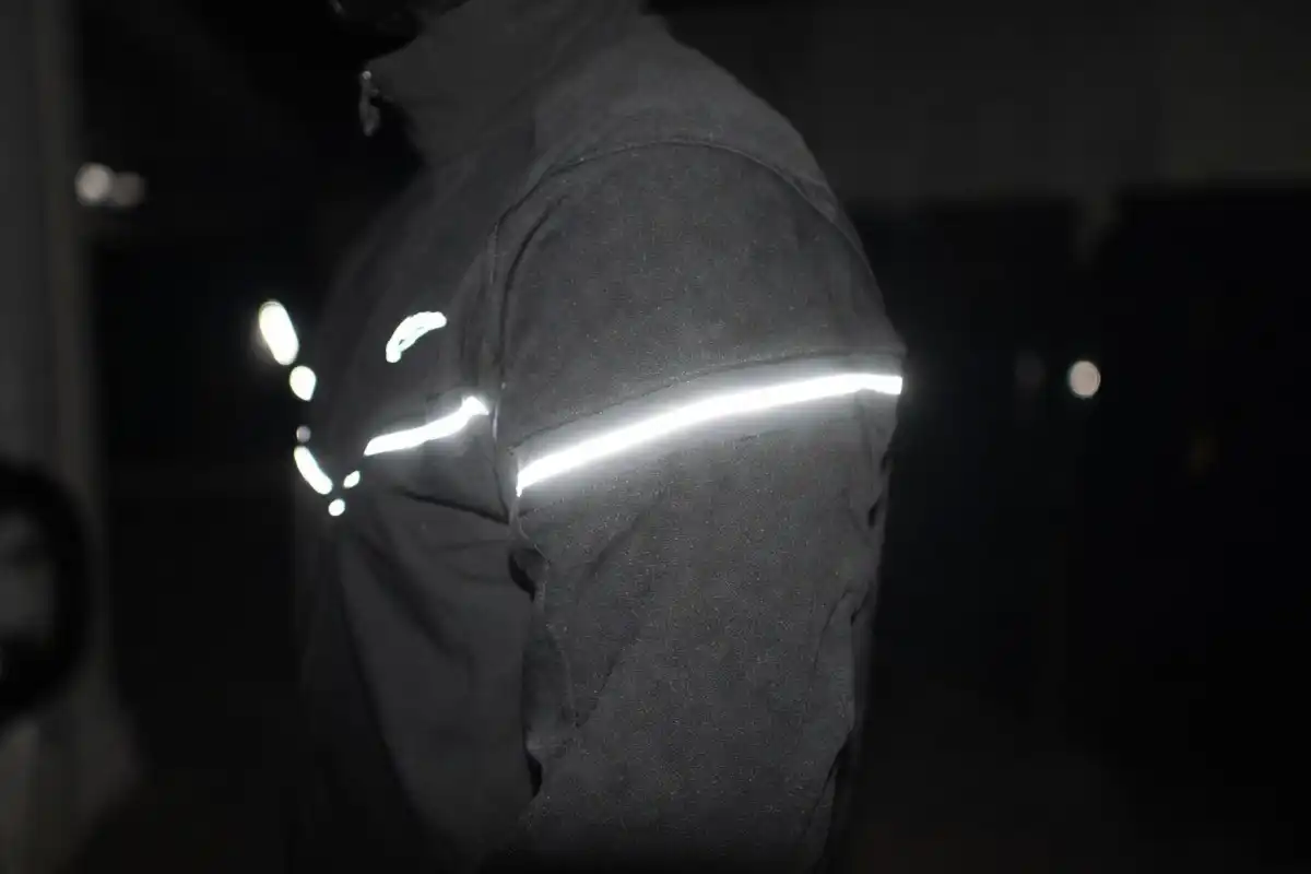 Close-up of a Nike Tech jacket sleeve showing retroreflective strip catching light in darkctive strip catching light in darkness