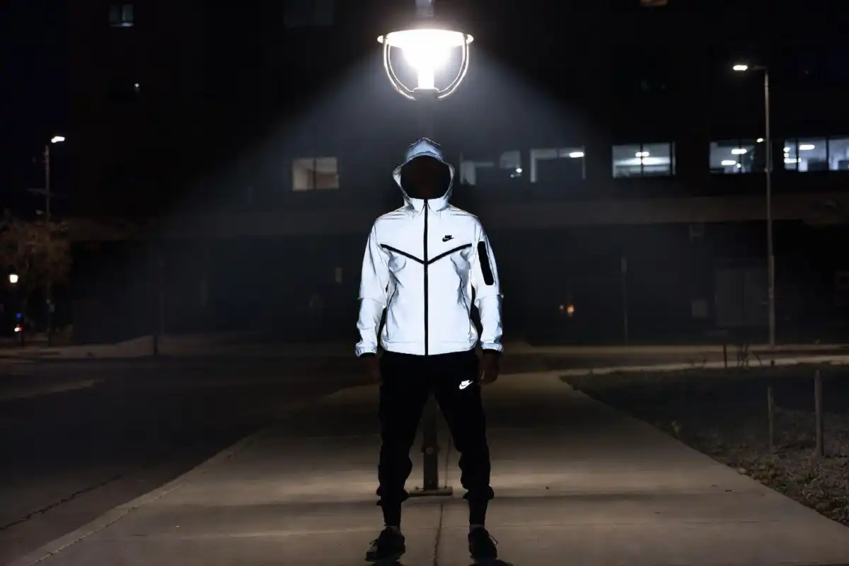 Athlete in a Nike Tech hoodie and jogger set under a streetlight showing reflective detailing at nighters under a streetlight at night