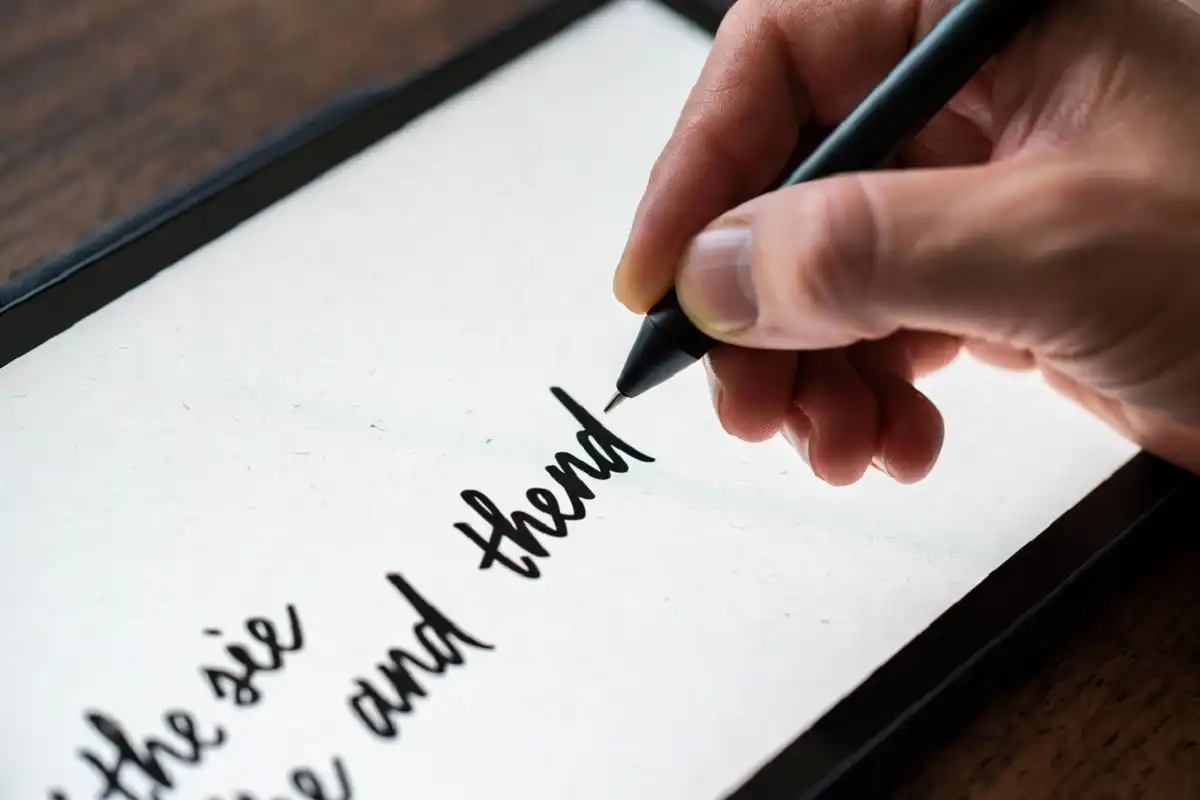 A hand writing cursive notes on a reMarkable 2 screen with a stylus showing the paper-like texture