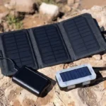 A collection of solar gadgets including a foldable solar panel, solar power bank, and solar lantern arranged outdoors on a sunny day