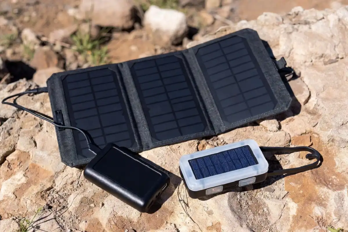 A collection of solar gadgets including a foldable solar panel, solar power bank, and solar lantern arranged outdoors on a sunny day