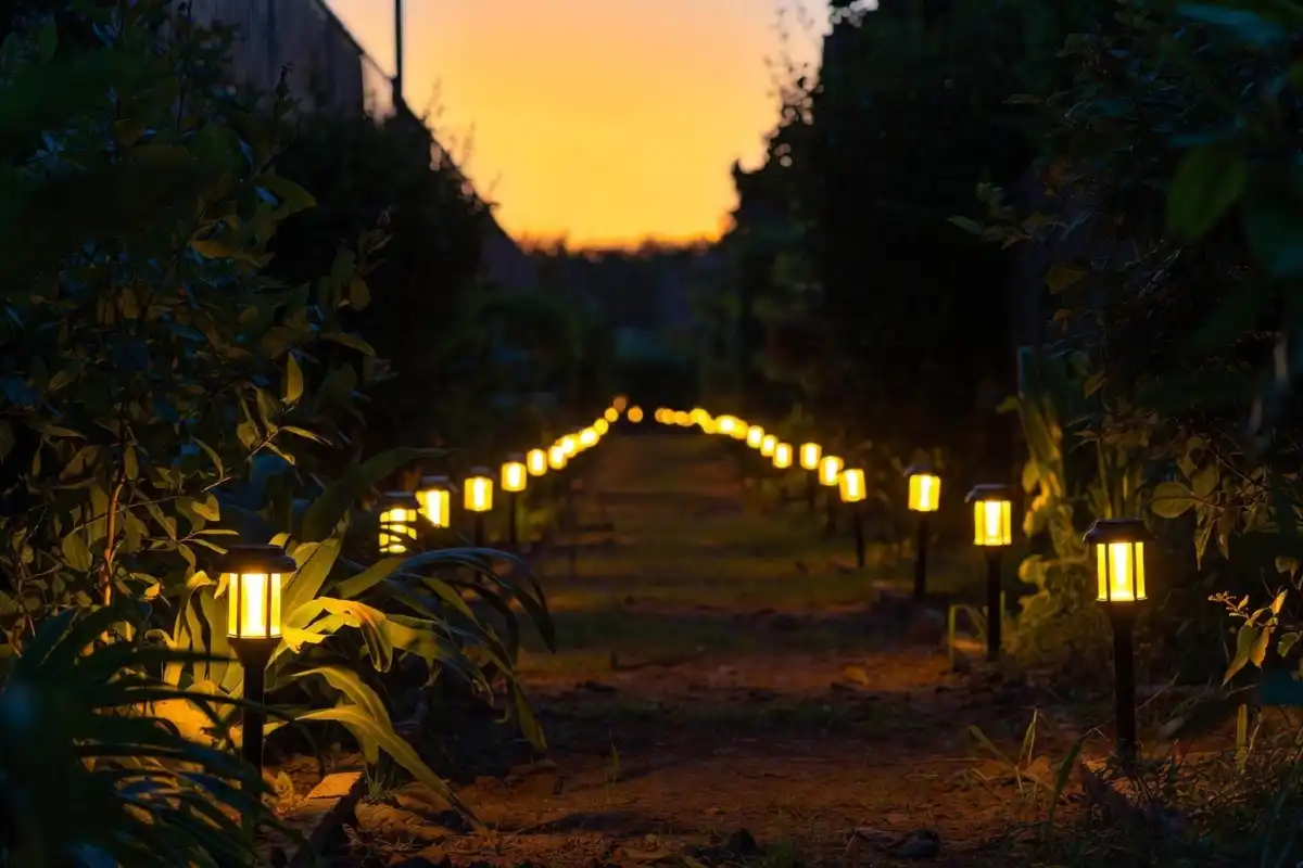 Solar-powered LED pathway lights glowing along a garden walkway at dusk with soft warm light and green plants on either side