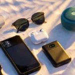 Collection of summer gadgets including neck fan, solar power bank, and waterproof speaker on beach sand