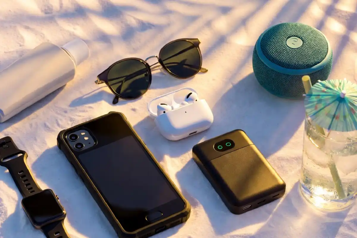 Collection of summer gadgets including neck fan, solar power bank, and waterproof speaker on beach sand