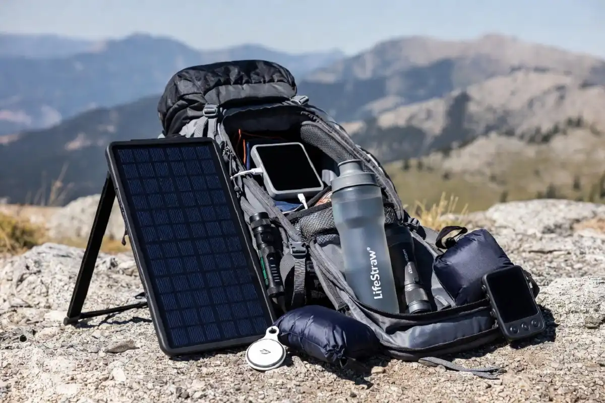 Adventure travel gadgets laid out on hiking backpack with solar charger water filter and tracker