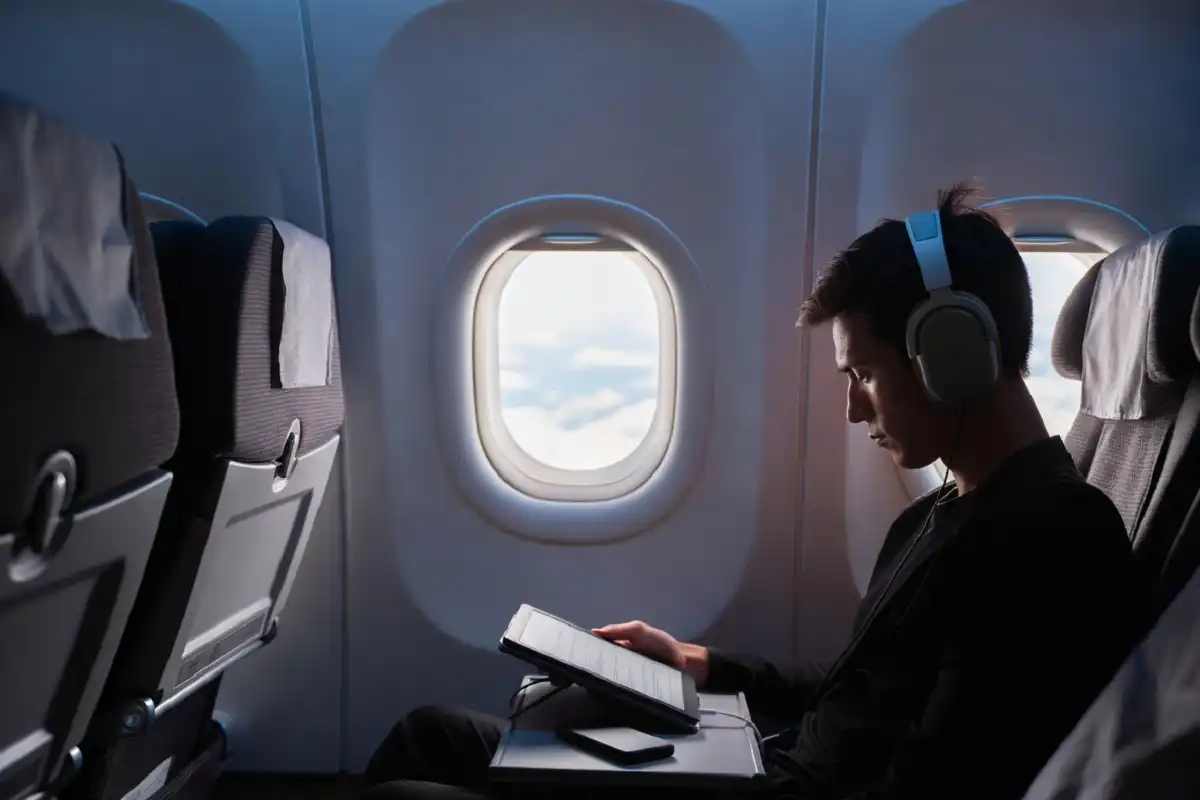 Traveler using travel gadgets on airplane including noise canceling headphones e-ink tablet and power bank