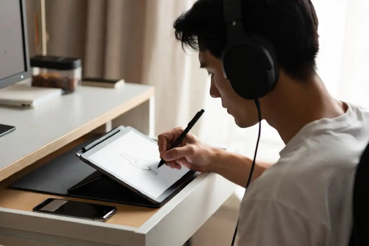 Person using a writing tablet and headphones in a distraction-free workspace