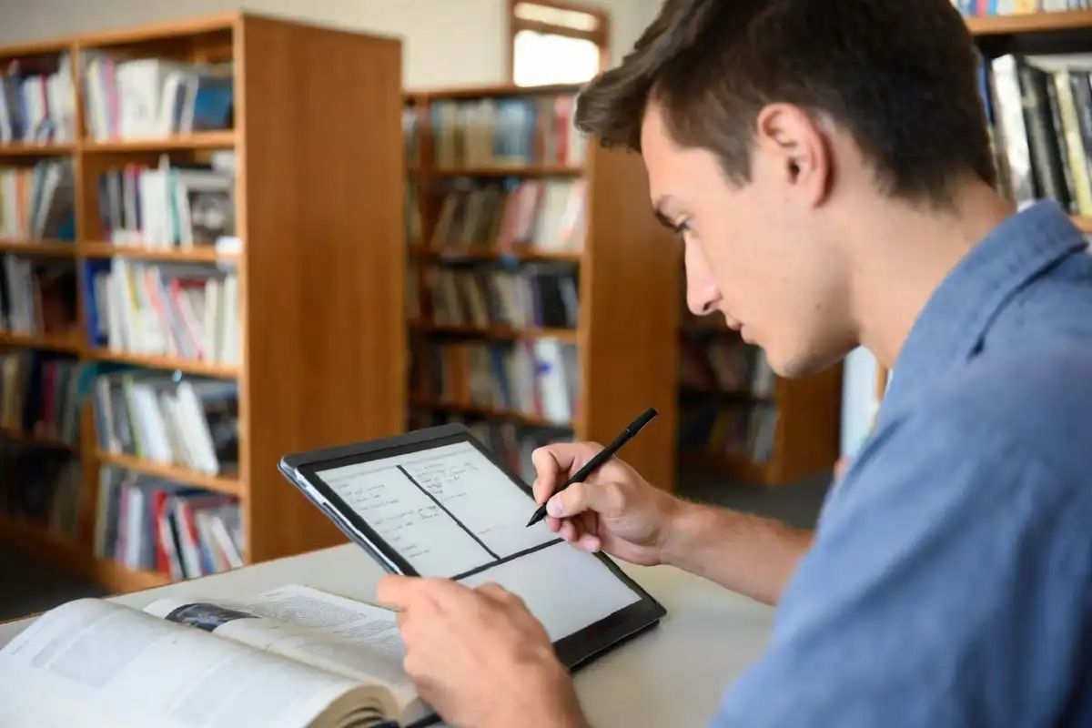 Student taking handwritten study notes on an e-ink tablet in a library